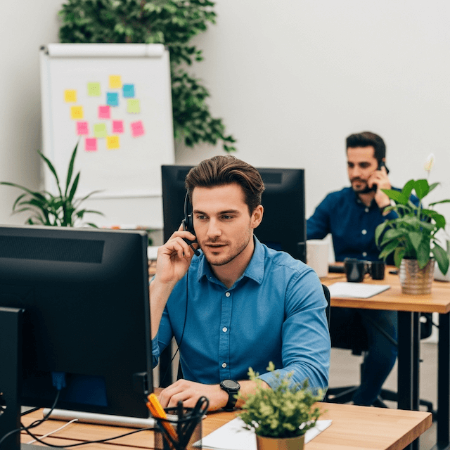 Zwei Männer am telefonieren Frau arbeitet vor einem Bildschirm mit Microsoft 365